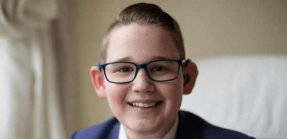 Photo of Reuben Litherland who received an invite to the Royal Wedding. Close up of face, smiling wearing hearing aids and glasses.