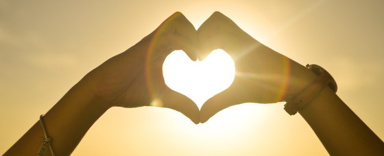 Picture of two hands joining together forming a heart shape against a sunset