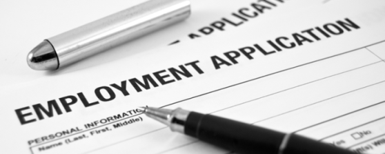 Close up of a piece of paper with 'EMPLOYMENT APPLICATION' written on it and also a pen is laying on it, with the lid above the paper on the table