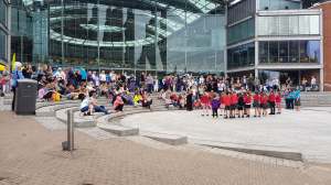 A crowd of people outside the Forum, Norwich watching a School Signing Choir