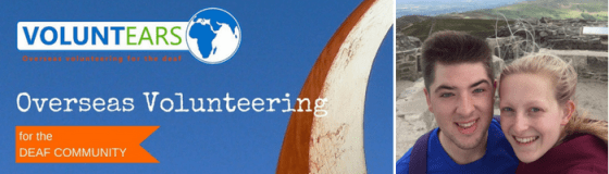 Banner. Left is the 'Voluntears' organisation logo which has a globe to the side of the name, underneath says 'Overseas Volunteering for the Deaf Community'. To the right is a photo of Dylan and I smiling on top of a hill.