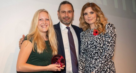 Me on the left, with a green lace dress, blonde hair smiling with a red trophy in my hand, with Mark Hopkinson in the middle wearing a black suit, white shirt and purple tie and Pip Tomson on the right wearing a black and white animal print dress and long brown wavy hair.
