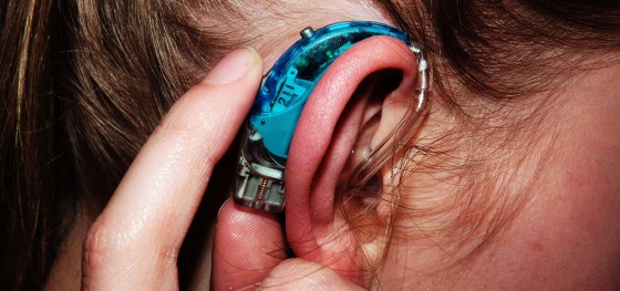 Close up of my turquoise hearing aid with my finger pressing a button