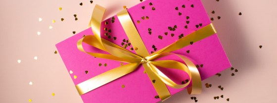 Pink wrapped present with gold ribbon round tied in a bow, covered in confetti