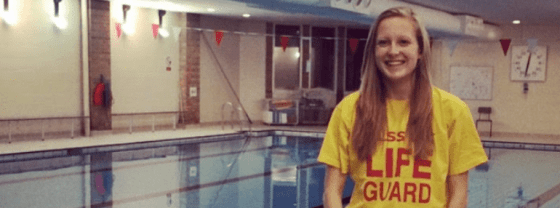 Me, a Deaf Pool Lifeguard in my yellow Lifeguard tshirt standing on poolside with the swimming pool behind me